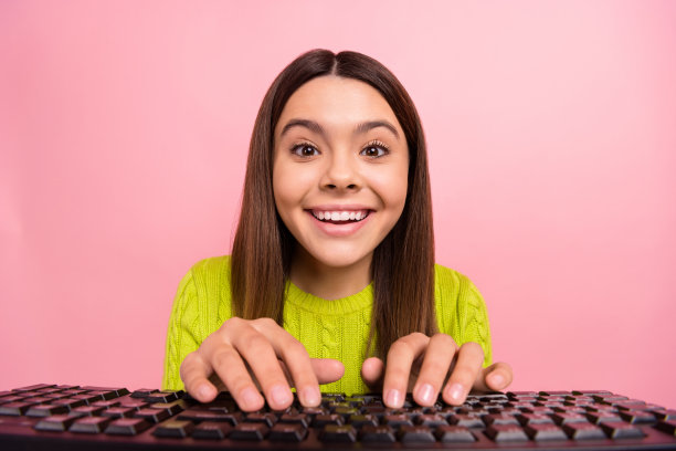 照片肖像漂亮的年轻女学生打字键盘聊天穿着时髦的绿色服装孤立在粉红色的背景图片下载