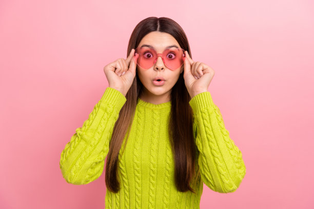 漂亮的年轻女学生印象深刻的照片肖像尝试粉红色的镜片眼镜，穿时髦的绿色服装孤立在粉红色的背景图片下载
