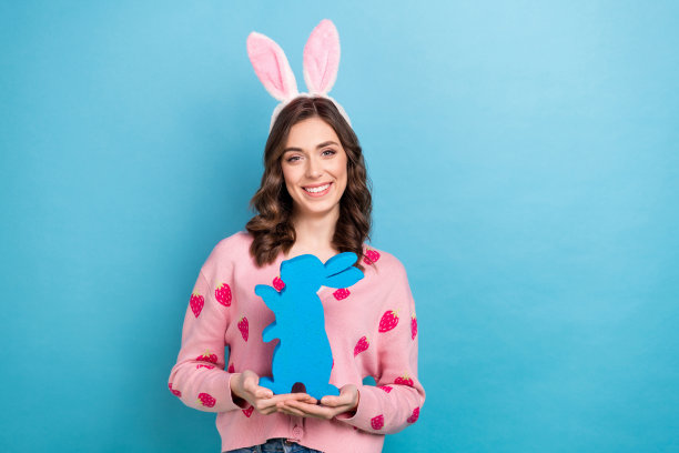 照片中开朗可爱的女士穿着粉红色的开衫复活节发带抱着兔子空的空间孤立的蓝色背景图片下载