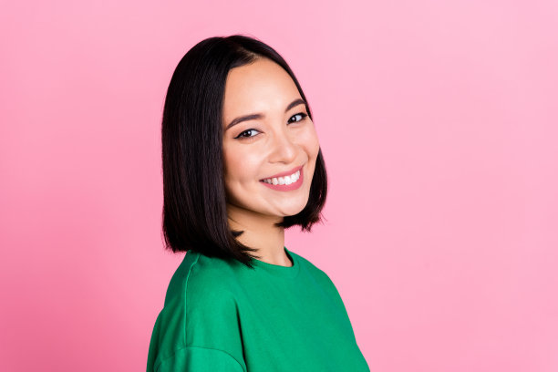 好心情的照片可爱的漂亮的女孩与鲍勃发型穿着绿色t恤牙齿微笑孤立在粉红色的背景图片下载