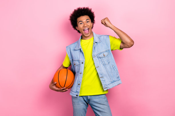 快乐时髦的人拿着篮球举起拳头成就运气的照片孤立在粉红色的背景上图片下载