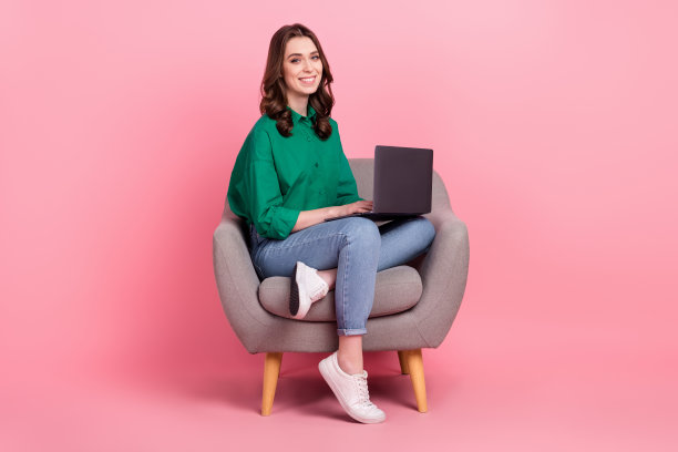 迷人的正面女士穿着绿色衬衫的全长照片坐在沙发上打字电子邮件现代设备孤立的粉红色背景图片下载