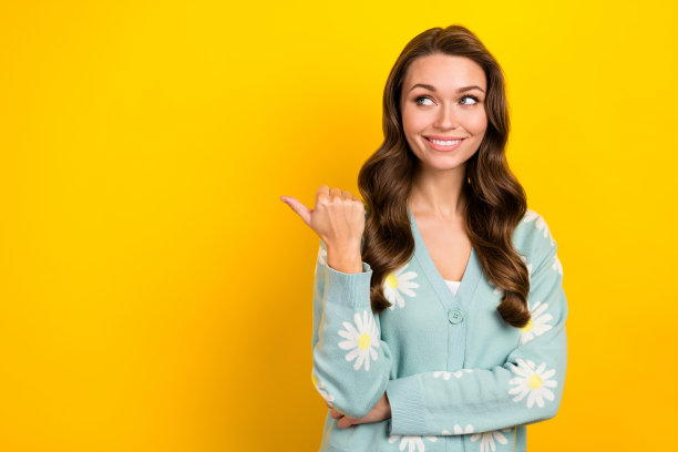 照片中闪亮梦幻的女人穿着绿松石开衫，手指指向空白的空间，孤立的黄色背景图片下载