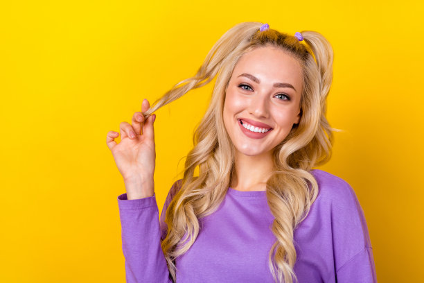 可爱的年轻女士的照片肖像拿着一缕洗发水卷发，穿着时尚的紫色衣服，孤立在黄色背景上图片下载
