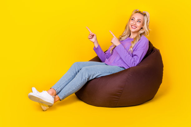 漂亮的年轻女孩的全尺寸照片豆袋手指看点空穿时髦的紫色衣服孤立在黄色的背景图片下载