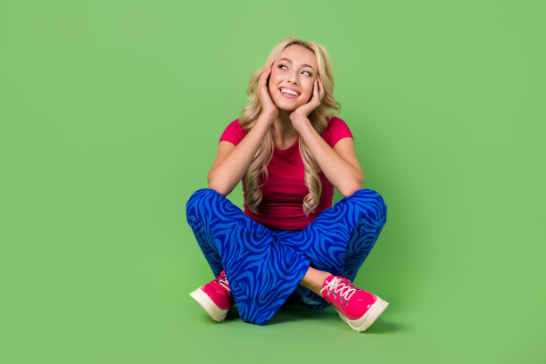 积极的女士的全身照片，坐在地板上，双手触摸脸颊，在绿色背景上看起来空白图片下载