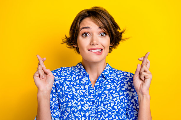 照片可疑有趣的女人穿着蓝色衬衫咬嘴唇交叉手指孤立黄色背景图片下载