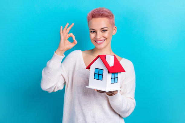 年轻的促销员房地产经纪人的照片显示好的标志，粉红色染的头发持有纸房子新财产孤立在青色背景图片下载