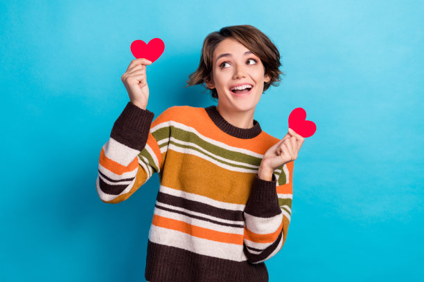 照片中可爱可爱的女士穿着条纹毛衣上升两个红色的小心脏，看起来空白的空间孤立的蓝色背景图片下载