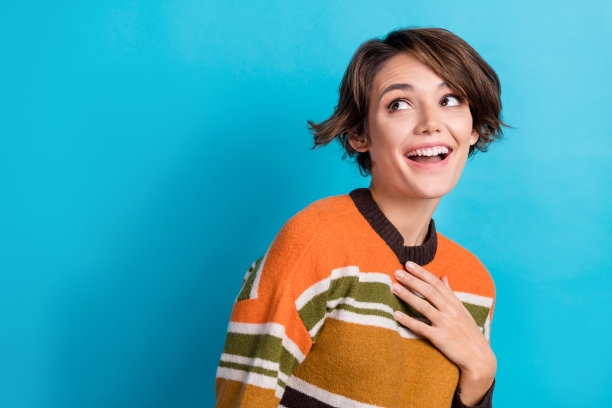 照片中兴奋时髦的女人穿着条纹套头衫，回头看空旷孤立的蓝色背景图片下载