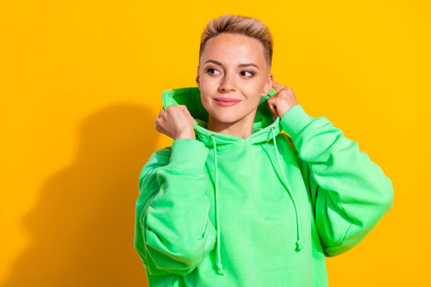 漂亮的年轻时髦的商业女博主的照片穿着绿色时尚的连帽衫触摸衣服看起来空白空间信息孤立在黄色背景图片下载