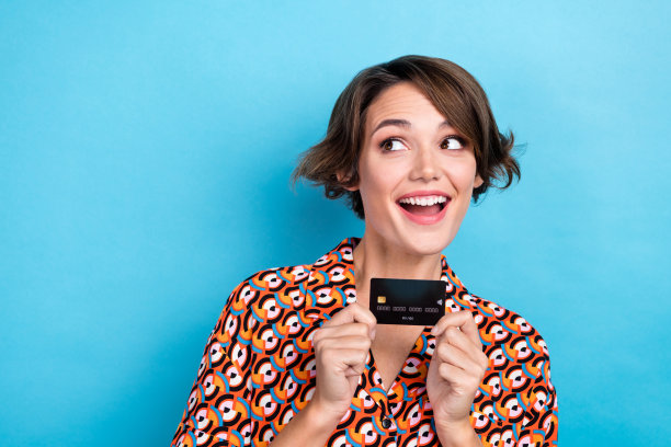 照片中可爱的兴奋的女人穿着印花衬衫上升信用卡看起来空的空间孤立的蓝色背景图片下载