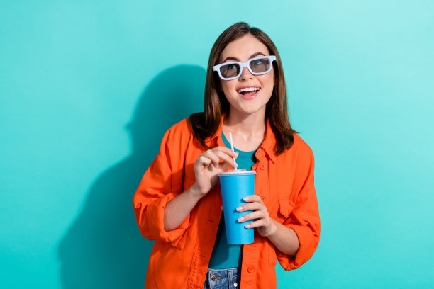 照片中可爱可爱的女友穿着时髦的橙色衣服感兴趣的看空空间门票销售孤立的青色背景图片下载