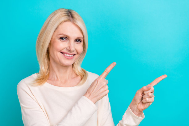 照片正面漂亮的女士穿着白衬衫指着两个手指空的空间孤立的蓝绿色背景图片下载