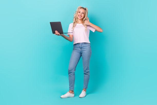正面漂亮女孩的全尺寸照片使用上网本演示拇指向上隔离在绿松石色背景图片下载