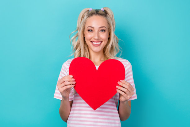 照片的快乐华丽的女士穿着条纹衣服，拿着红色的纸卡宣传诊所孤立的青色背景图片下载