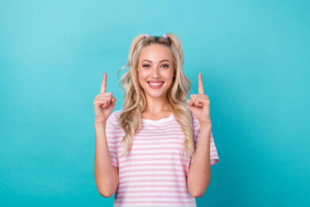 照片中开朗可爱的女孩露出牙齿微笑，手指指向上方，空白的空间孤立在海蓝宝石的背景上图片下载