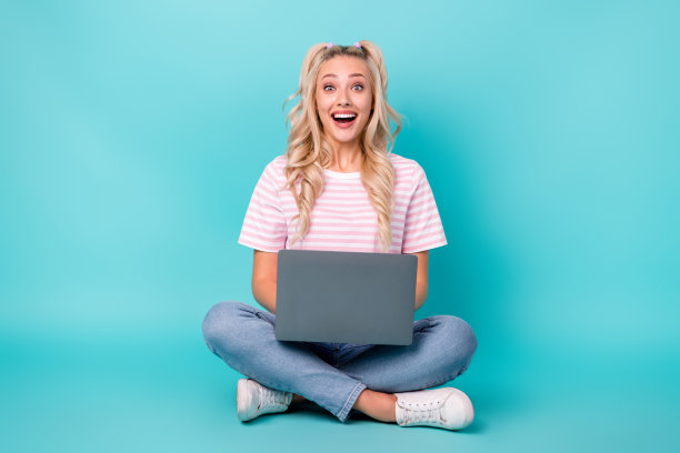 震惊的可爱女士的全身照片坐在地板上，用上网本张开嘴孤立在绿松石色背景上图片下载