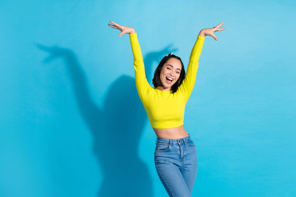 中国年轻人粗心的苗条女士跳舞的照片，举起双手，穿着时尚迷人的节日服装，孤立在蓝色的背景下图片下载