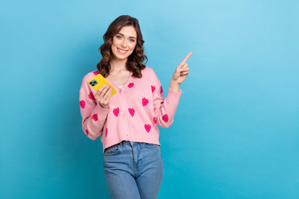 可爱的女士手持小工具点空的照片肖像穿着时髦的粉红色草莓印花服装孤立在蓝色的背景图片下载