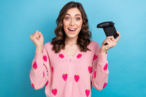 照片的幸运时髦的女人穿粉红色的开襟毛衣上升拳头赢得游戏孤立的蓝色背景图片下载