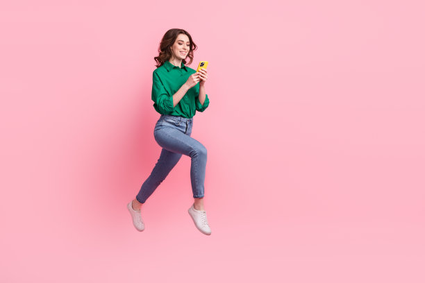 正的全尺寸照片华丽的无忧无虑的女孩穿牛仔裤绿色衬衫跑快看智能手机孤立在粉红色的背景图片下载