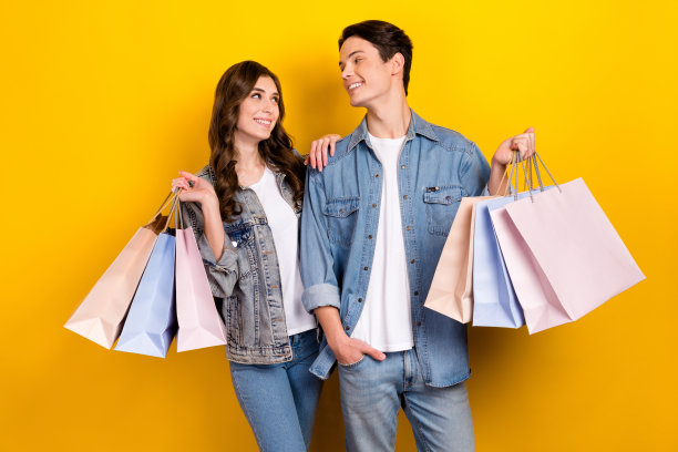 照片中，两个可爱的人相视而笑，拿着购物袋孤立在黄色背景上图片下载