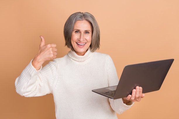 照片中的漂亮自信的女人穿着针织套头衫，拇指朝上聊天，现代小工具孤立的米色背景图片下载