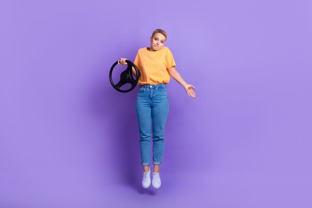 全身照片困惑犹豫的女孩穿着白色运动鞋牛仔裤裤子拿着方向盘孤立的紫罗兰色背景图片下载