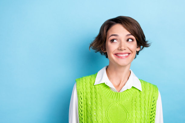 照片漂亮可爱的满意有趣的女人与鲍勃发型穿着绿色马甲看起来空白空间孤立的蓝色背景图片下载