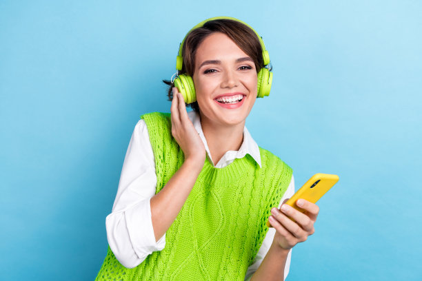 照片可爱的积极的女士穿着时髦的绿色衣服享受新的打击质量的声音耳塞孤立的青色背景图片下载