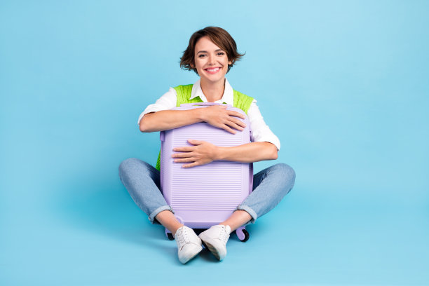 长照片的好心情的女人与鲍勃发型穿着绿色马甲拥抱手提箱孤立的蓝色背景图片下载