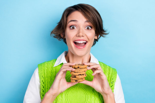 照片中开朗积极的女士穿着绿色时尚的衣服，拿着美味的食物，在青色的背景上享受休息，暂停午餐图片下载