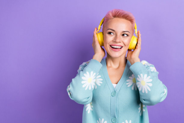 漂亮的短发女人穿着蓝色开襟羊毛衫的照片，双手触摸耳机，在紫色的背景上看起来空空荡荡图片下载