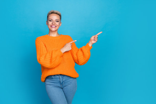 照片中迷人的年轻女子的肖像点空模特欢快地穿着时髦的橙色衣服孤立在蓝色的背景图片下载