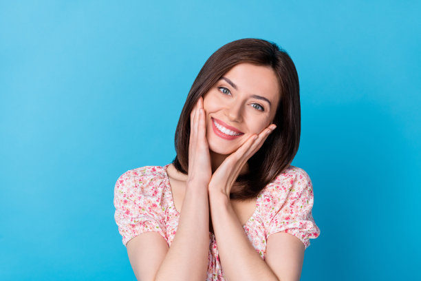 年轻可爱的漂亮女人的特写照片触摸颧骨微笑爱自己干净的皮肤脸孤立的蓝色背景图片下载