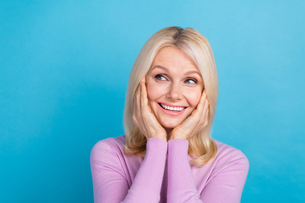 照片正面华丽的女士穿着时尚的衣服，手臂触摸脸颊，看起来空的空间有趣的提供孤立的蓝色背景图片下载