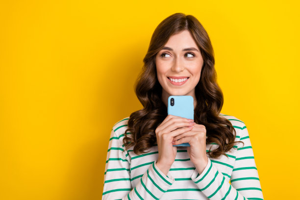 照片中的美女手持设备，看起来好奇的空白空间穿着时尚的条纹装孤立在黄色的背景图片下载