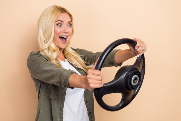 照片中，迷人的喜出望外的女士穿着时尚的衣服，看起来空旷的新道路上的速度试驾孤立的米色背景图片下载