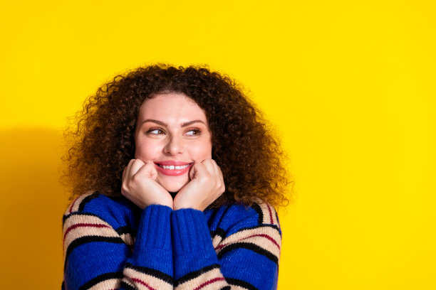 照片中乐观的女人有着烫发的发型，穿着温暖的毛衣，在黄色的背景上提供了孤立的空间图片下载