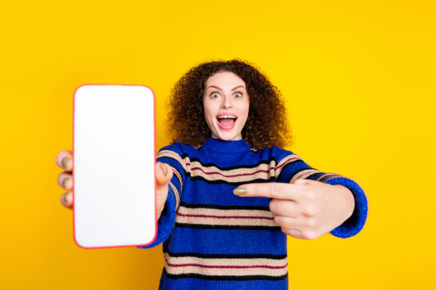 照片中，穿着毛衣的女孩穿着烫发的衣服，在黄色背景的智能手机屏幕上指示菜单图片下载