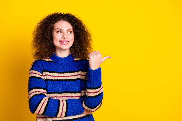 照片中穿着温暖的毛衣的可爱的女人穿着烫发的头发，在黄色的背景上看起来像是在销售空白的空间图片下载