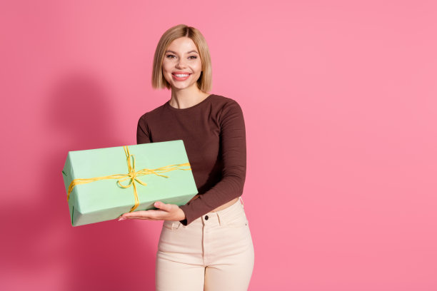 照片中可爱的漂亮可爱的女孩穿着时髦的棕色衣服，拿着礼物，在粉红色的背景上孤立起来图片下载