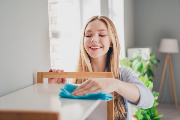 照片积极的好心情的女孩穿着蓝色衬衫做家务擦拭架子在室内房子公寓房间图片下载