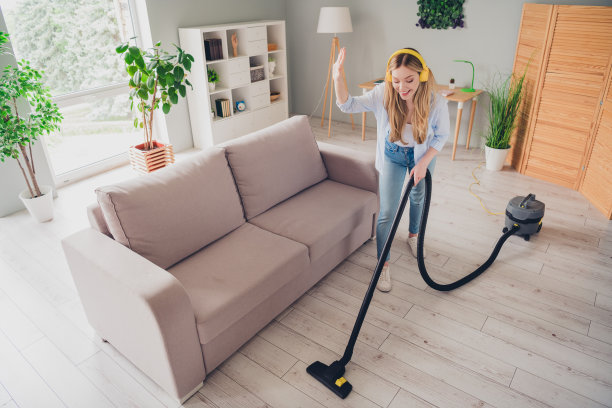 照片中无忧无虑开朗的年轻女士穿着休闲衬衫享受音乐，在室内房间、家里、房子里吸尘图片下载