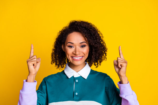 照片积极漂亮的女人与卷发穿着条纹上衣，在黄色背景上提供孤立的空间图片下载