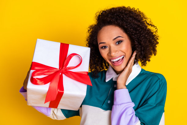 照片肖像迷人的年轻女子拿着惊喜的礼物盒穿着时尚的条纹衣服孤立在黄色背景图片下载