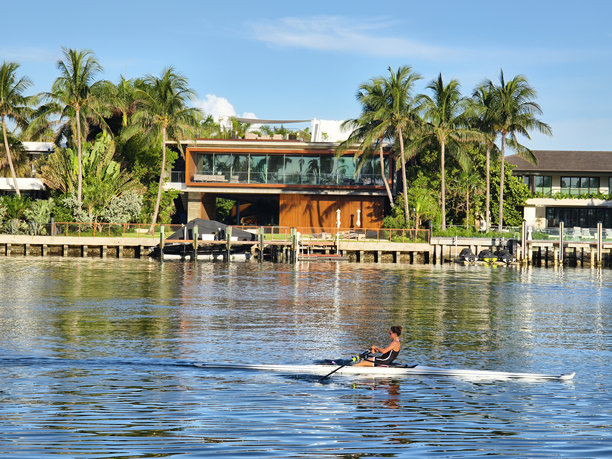 迈阿密海滩，佛罗里达州——一个女子独木舟在印第安河上疾驶，在一个阳光明媚的日子里，背景是豪华的豪宅。图片下载