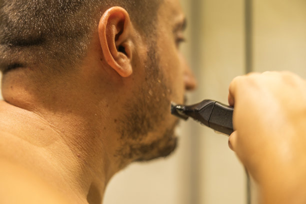 近距离拍摄的照片显示，这个体型过大的男人站在浴室里，用电动剃须刀刮胡子。图片下载