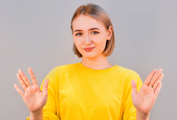 年轻漂亮的女人穿着黄色的毛衣，在灰色的背景上做着停车标志。特写照片。请冷静下来。别担心图片下载